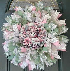 a pink and green christmas wreath with a snowman on the top, surrounded by ribbons