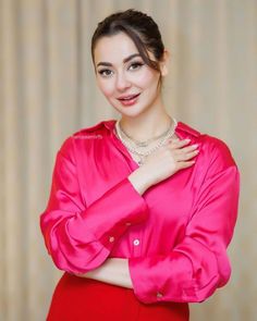 a woman in a pink shirt and red skirt posing for the camera with her hands on her chest