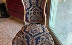 an ornately decorated chair sitting in front of a window next to a red dresser