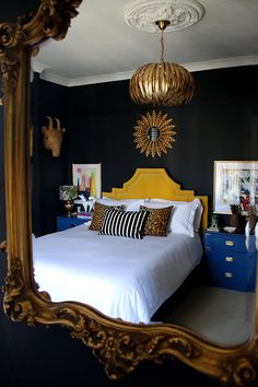 a bedroom with black walls and gold framed mirror on the wall above it is a bed with white sheets and pillows