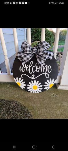 a welcome sign on the front porch with daisies and plaid bow hanging from it