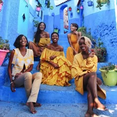 four women in yellow dresses are sitting on the steps and smiling at the camera, with potted plants behind them