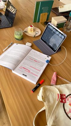 an open book sitting on top of a wooden table next to a laptop and other items