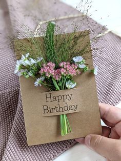 a person holding a card with flowers on it that says happy birthday in front of them