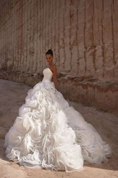 a woman in a white wedding dress standing by a stone wall with her hands on her hips