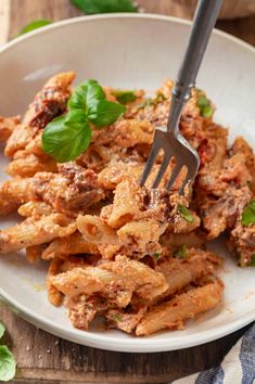 a white plate topped with pasta covered in sauce and basil leaves next to a fork