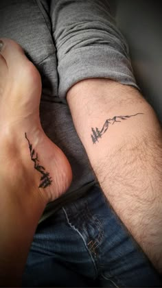 two people with matching tattoos on their arms, one is holding the other's leg