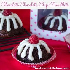 chocolate cupcakes with white icing and raspberries on top, sitting on a red tablecloth