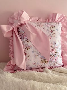 a pink pillow with a large bow on the front and back of it sitting on a bed