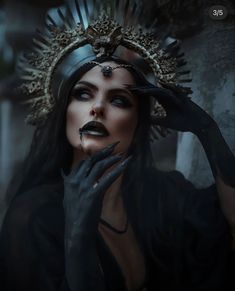 a woman with dark makeup and black gloves holding her hands up to her face while wearing a headdress