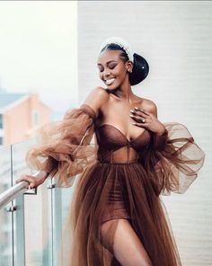 a woman in a brown dress posing on a balcony with her arms around her waist