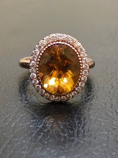 an oval shaped yellow sapphire and diamond halo ring on top of a black countertop