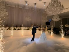 a bride and groom dance in the middle of a cloud filled ballroom with chandeliers hanging from the ceiling