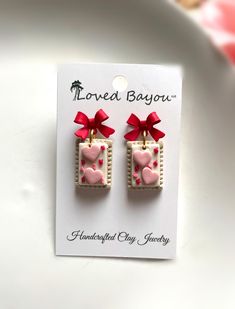 -made with polymer clay -hypoallergenic hardware -custom, one of a kind -complimentary pair of mini stud earrings included with every order Everyone loves a sweet treat!! Especially a Valentine's Day pop tart! These adorable miniature food earrings look good enough to eat. Frosted with hearts and sprinkles, these danish delights are hanging gently from a red bow. They are super lightweight and minimalistic. They add the perfect touch of pop and color. Eat these before they're gone :)  1" in length and .5" in width. Jewelry hardware is hypoallergenic, lead, and nickel free. Comes with 2 hypoallergenic silicone backings. Polymer clay should never be dropped or bent. Please refrain from excessive moisture as this damages integrity of hardware. If clay becomes soiled, please wipe gently with m Pop Tart, Valentines Day Cookies, Food Earrings, Cookie Frosting, Mini Studs, Bow Earrings, Miniature Food, Sweet Treat, Red Bow