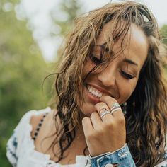 a woman smiles as she holds her hand up to her face and wears a ring