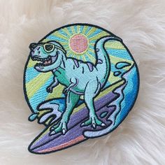 a patch with a dinosaur riding a surfboard in the sun on top of white fur