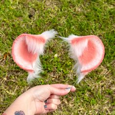 a hand holding two pink ears with white feathers