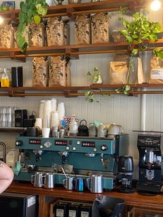 a woman standing in front of a coffee machine with plants growing on the wall behind it