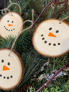 three wood slices with snowmen painted on them hanging from the branches of a christmas tree