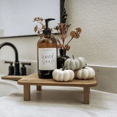 a bottle of hand soap sitting on top of a wooden tray next to white pumpkins