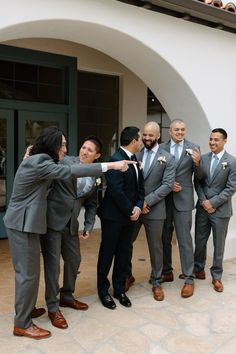 a group of men standing next to each other in front of a white wall and building