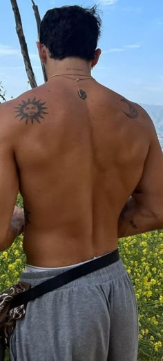 the back of a man with tattoos on his upper and lower half, standing in front of yellow flowers