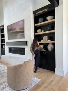 a woman standing in front of a book shelf filled with books and vases next to a fireplace