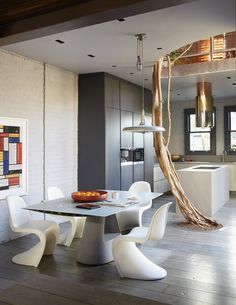 a dining room table with white chairs and a bowl of fruit on the plate next to it