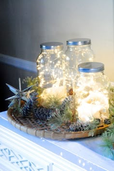 two mason jars filled with lights sitting on top of a wooden tray covered in snow