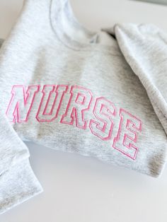 two sweatshirts with the word nurse embroidered on them sitting next to eachother