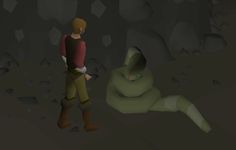 a man standing next to a giant green creature in a dark cave with rocks on the ground