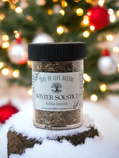 a jar of winter solstice sits in front of a christmas tree