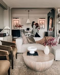 two women walking through a living room with couches, chairs and coffee table in front of them