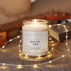 a white tea candle sitting on top of a table next to a string of lights