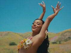 a woman in a hula skirt with flowers on her chest and arms raised up to the sky