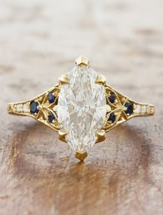 an oval cut diamond with blue sapphire accents sits on top of a piece of wood