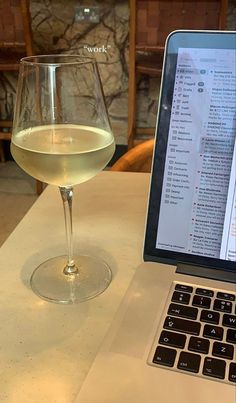 an open laptop computer sitting on top of a table next to a glass of wine