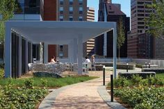 people are sitting at tables and chairs in a park with tall buildings behind them on a sunny day