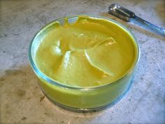 a bowl filled with yellow liquid sitting on top of a counter next to a spoon