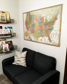 a black couch with a map on the wall above it and bookshelves behind it