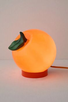 an orange shaped lamp with a green leaf on it's tip, sitting on a white surface