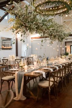 a long table with white linens and greenery hanging from it's ceiling