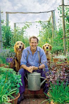 a man and two dogs are sitting in the garden holding a watering can with plants