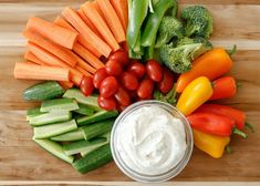 vegetables and dip in a bowl on a cutting board next to carrots, broccoli