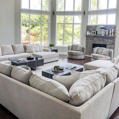 a living room filled with lots of furniture in front of large windows and a fire place