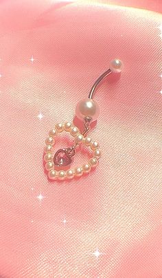 a pink heart shaped belly ring with pearls and a hello kitty brooch on it