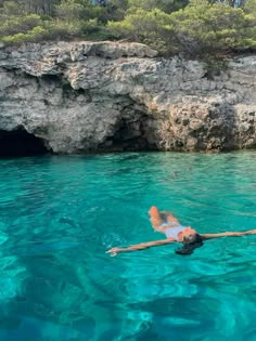 a person floating in the water next to a rocky cliff and blue lagoon with clear waters