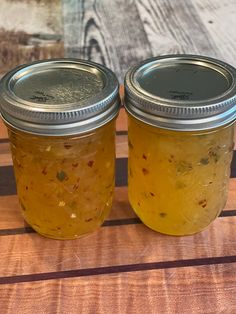 two jars of pickles sitting on top of a wooden table next to each other