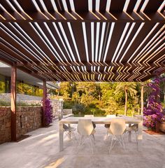 an outdoor dining area with table and chairs under a pergolated roof over a stone patio