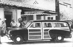 an old black and white photo of people standing in front of a car with the door open